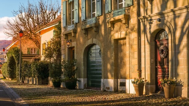 A historic building with arched doorways, a green door, and a balcony with a wrought iron railing. - Casa Vinitoscani (Perroy)
