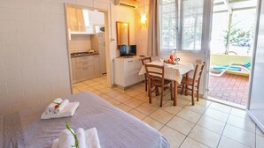 Habitació d'hotel amb llit, taula de dinar amb cadires, cuina americana i balcó amb piscina.