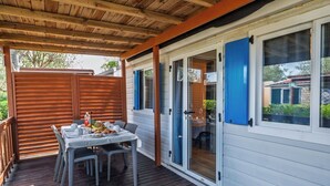 A covered outdoor dining area with a table set for four, wooden deck flooring, and a view of the surrounding neighborhood. - Lovely apartment in villa for 5 guests with A/C, pool, WIFI, TV and terrace (Rosolina)