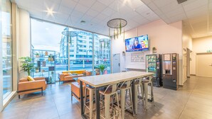 A modern hotel lobby with a large window, seating area, a bar, a TV screen, and vending machines. - Break & Home Paris Italie Porte De Choisy (Ivry-sur-Seine)