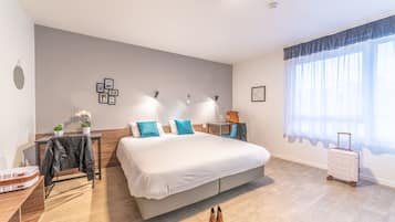 Ett modernt hotellrum med en stor säng, ett skrivbord, en stol, en resväska och ett fönster med gardiner.