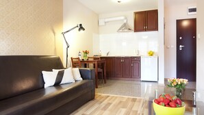 Un soggiorno moderno con un divano in pelle scura, un tavolino in vetro con una ciotola di fragole, una zona pranzo con un tavolo e sedie in legno e una cucina con mobili in legno ed elettrodomestici bianchi.