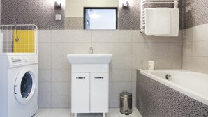 Un bagno moderno con lavatrice, lavandino con specchio, vasca e un piccolo cestino.
