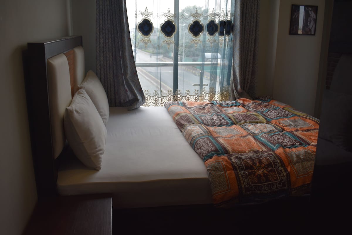 Un dormitorio con cama, ventana con cortinas y vista a la calle.