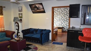 A living room with a blue sofa, a red armchair, a coffee table, and a kitchen area with a black countertop and red bar stool. - River View Residency (Rawalpindi)