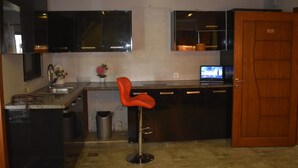 A modern kitchen with black cabinets, a stainless steel sink, a red bar stool, and a television on the counter. - River View Residency (Rawalpindi)