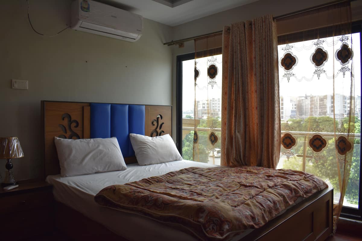 Un dormitorio con una cama grande, un cabecero, una ventana con cortinas y vistas a edificios.