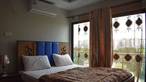A bedroom with a large bed, a headboard, a window with curtains, and a view of buildings outside. - River View Residency (Rawalpindi)
