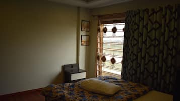 A bedroom with a bed, a nightstand, a window with curtains, and a wall with two framed pictures.