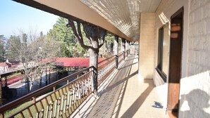 Un balcone coperto con vista su alberi e un edificio con tetto rosso.