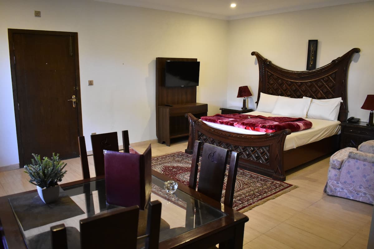 A bedroom with a bed, a TV mounted on the wall, a wooden headboard, a bedside table, and a chair.