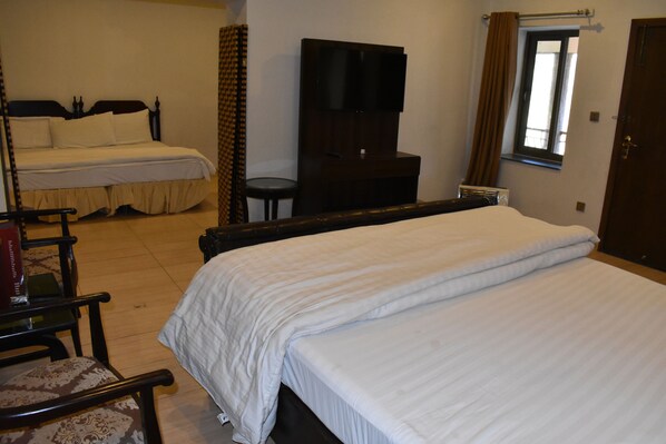 A hotel room with two beds, a television, a window, and a desk with a chair.