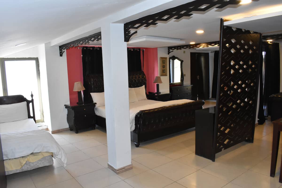 A spacious bedroom with a large bed, a nightstand, a dresser, and a decorative partition.