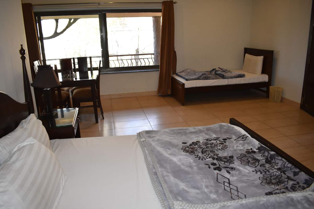 A hotel room with a bed, a desk, and a chair. There is a window with curtains, and a balcony is visible through the window.