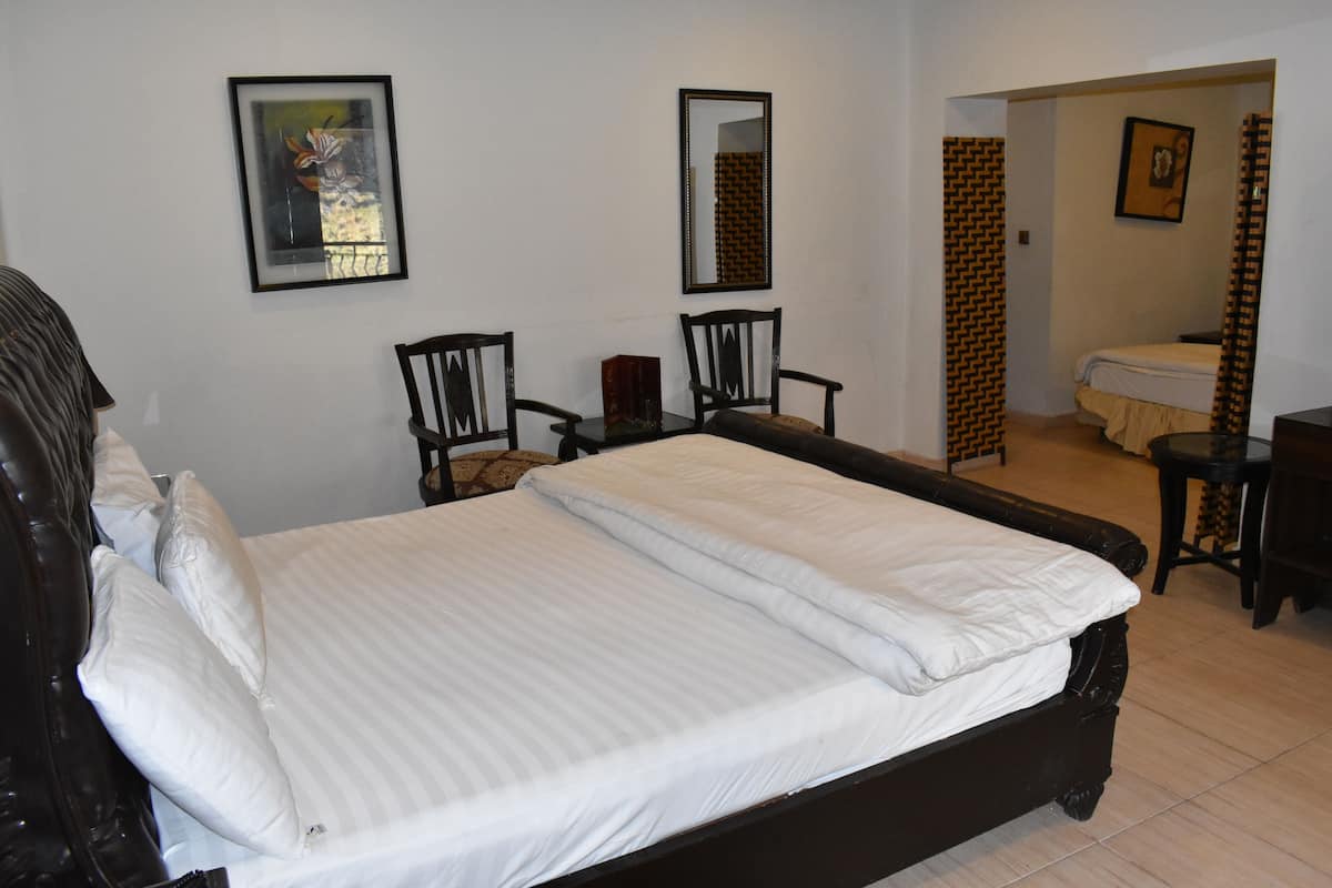 A neatly made bed with white linens, two chairs, a mirror, and a framed picture on the wall.