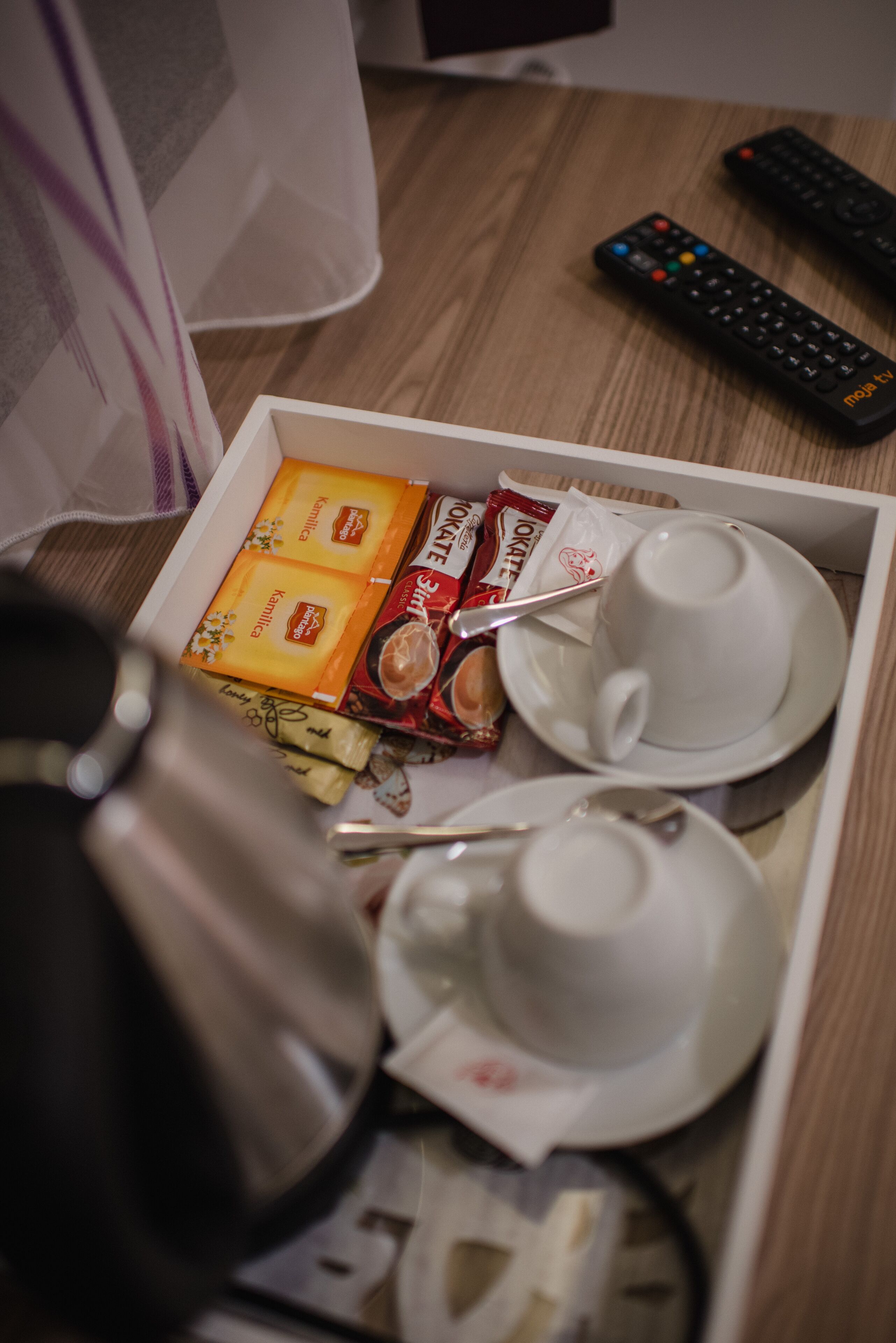 A tray with a cup, saucer, and a kettle, along with some packaged snacks and a remote control.