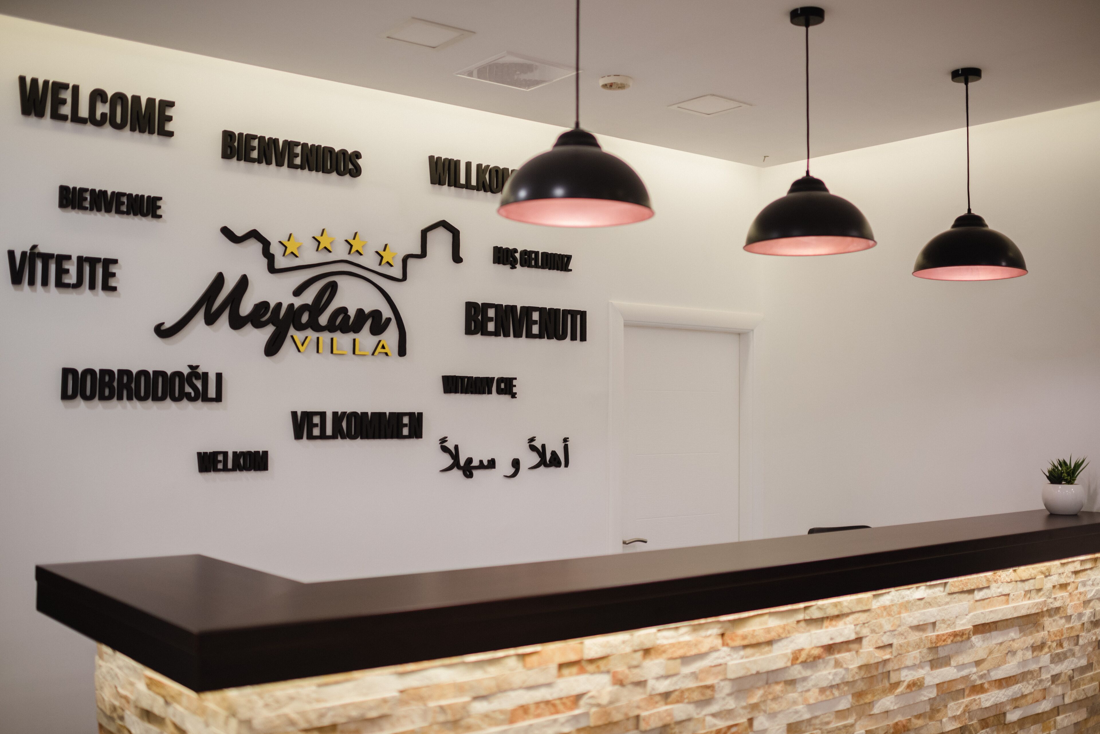 A reception area with a stone-textured counter and a wall displaying multilingual 'Welcome' signs.