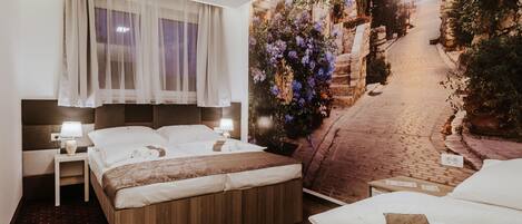 Ein Hotelzimmer mit einem großen Bett, einem Nachttisch mit Lampe und einem Wandbild einer Kopfsteinpflasterstraße mit Blumen.