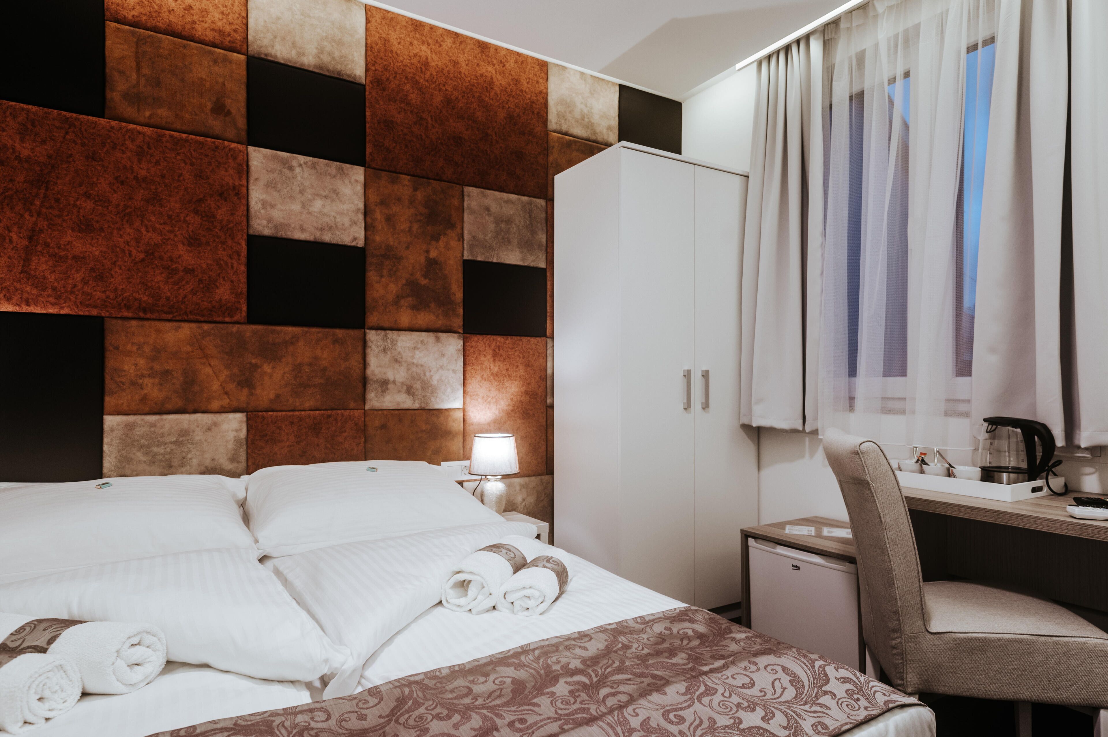 Habitación de hotel con cama, escritorio, armario y ventana con cortinas.
