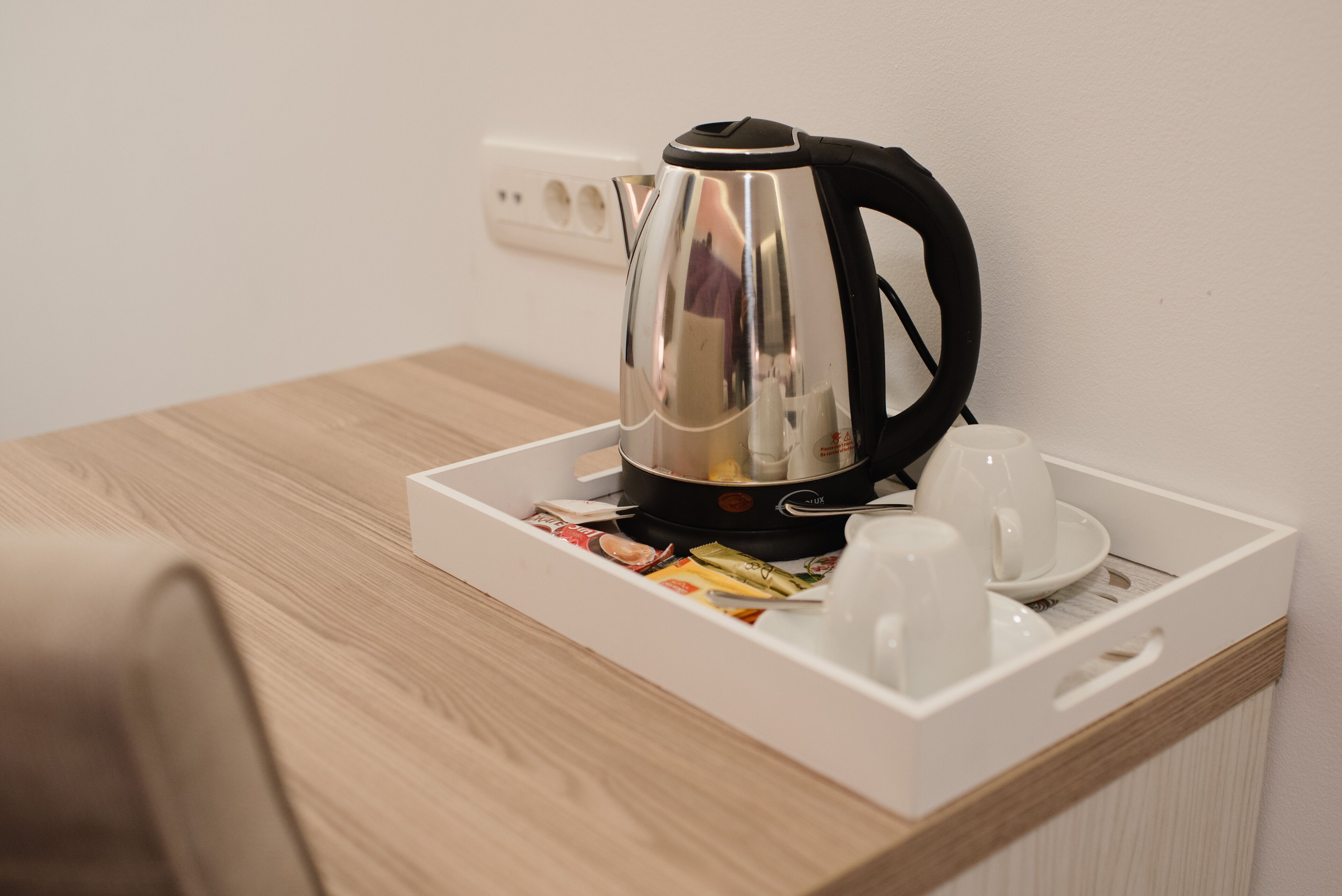 A stainless steel kettle on a tray with cups and snacks on a wooden table.