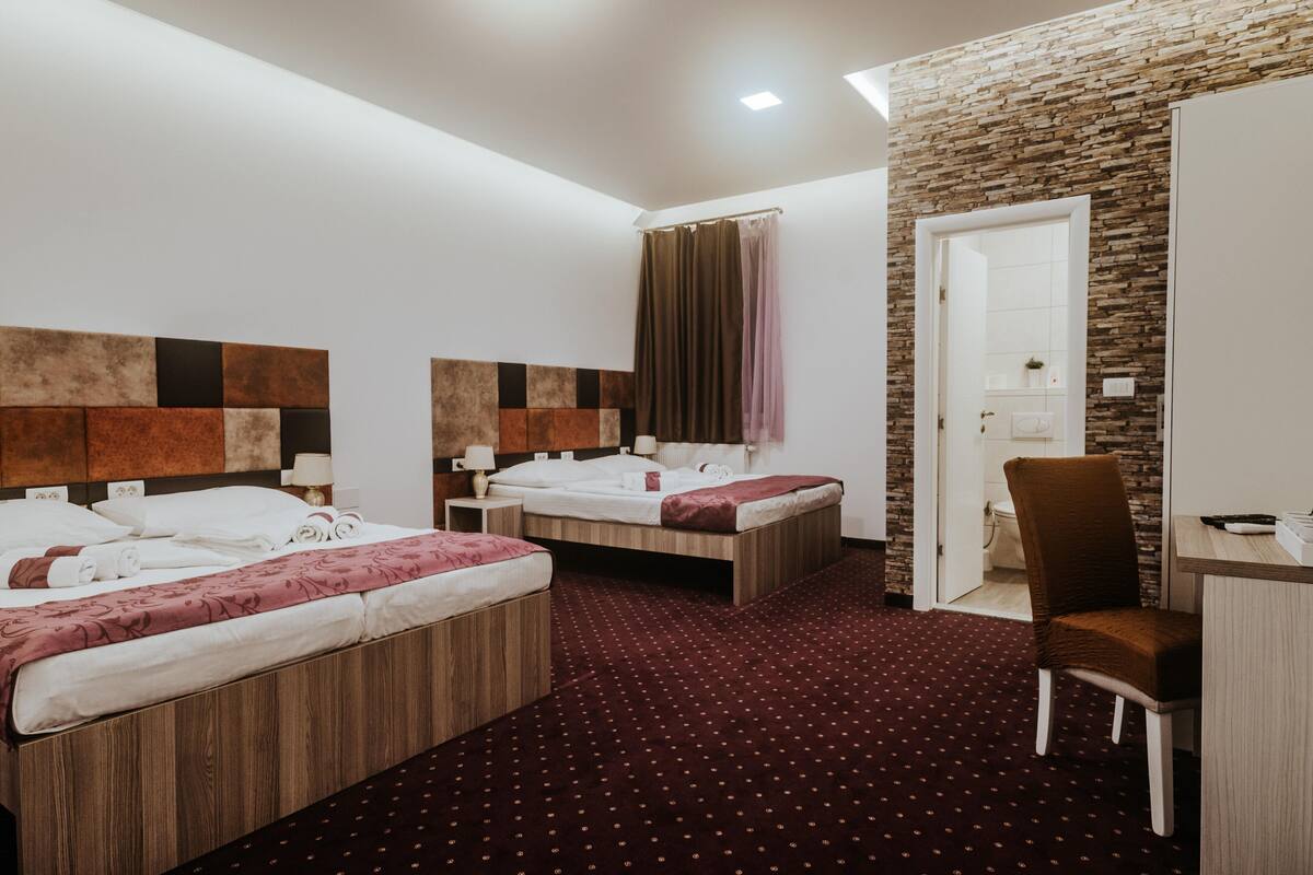 A hotel room with two beds, a desk, a chair, and a bathroom door.