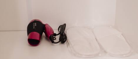 A pair of black and pink headphones with a cable, placed next to a pair of clear plastic slippers on a white surface.