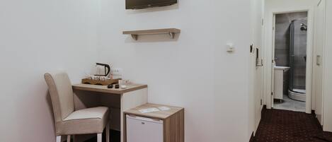 A compact room with a desk, chair, small refrigerator, mounted TV, and a shower area.