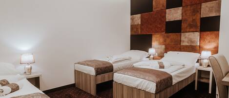 A hotel room with two single beds, a wooden headboard, a small table with a lamp, and a patterned carpet.