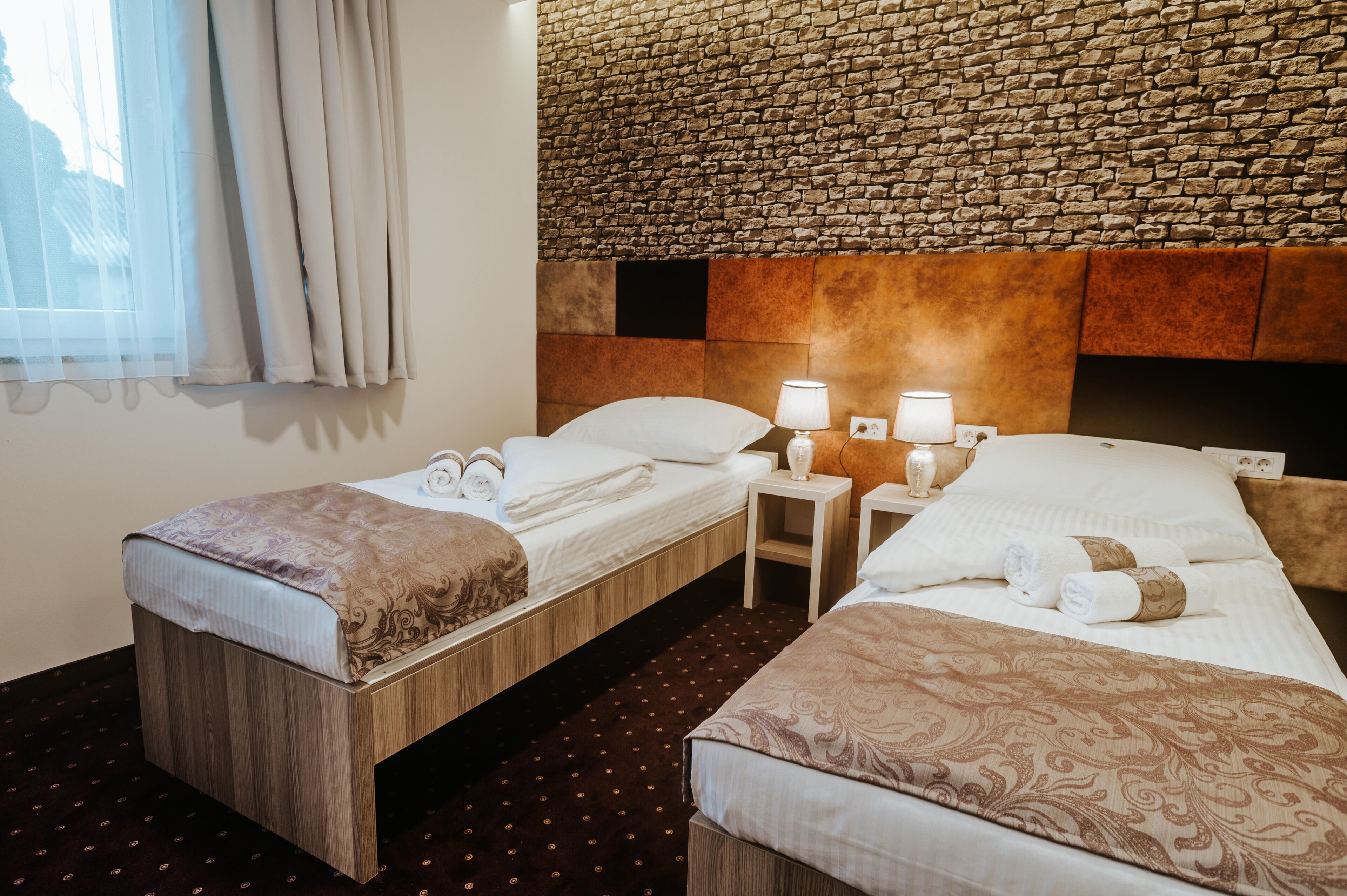 Quarto de hotel com duas camas de solteiro, parede de pedra e janela com cortinas.