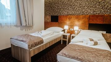 Quarto de hotel com duas camas de solteiro, parede de pedra e janela com cortinas.