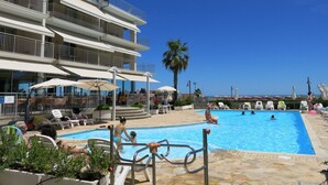 Zona de piscina con varios niveles de balcones, mobiliario exterior y cielo azul despejado.