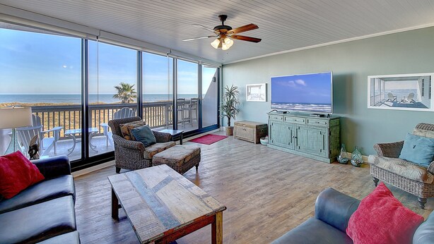 A spacious living area with a large window overlooking the ocean, a ceiling fan, and a television. - Ocean View Delight, Resort Pools, Private Boardwalk | MP301 (Port Aransas)