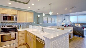 A modern kitchen with a large island, stainless steel appliances, and a view to the living area. - Ocean View Delight, Resort Pools, Private Boardwalk | MP301 (Port Aransas)