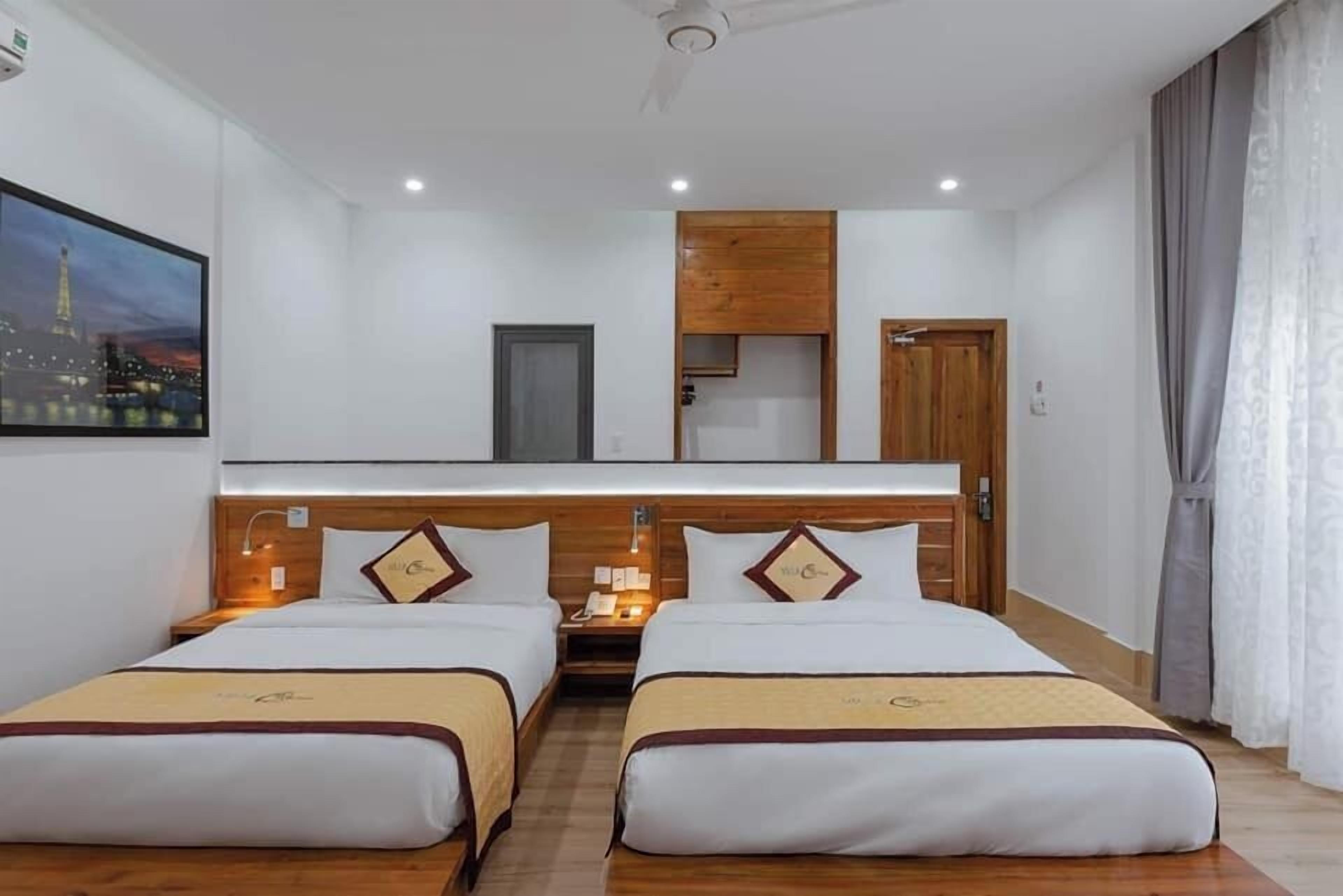 A hotel room with two beds, a wooden headboard, a nightstand, a mirror, a painting of a cityscape, and a window with curtains.