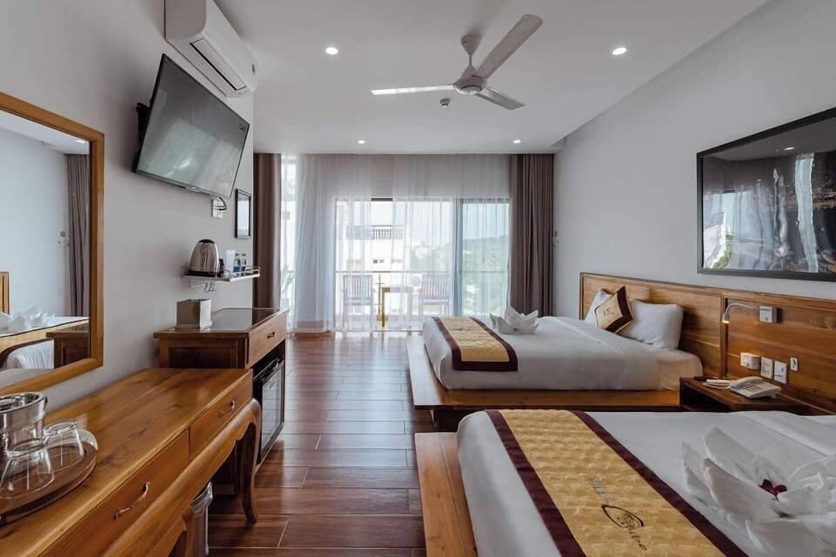 Ein Hotelzimmer mit einem Bett, einem Schreibtisch, einem Fernseher, einem Deckenventilator und einem großen Fenster.