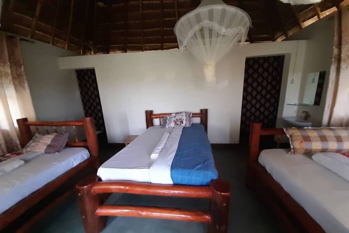 A room with two wooden beds, a mosquito net, and a bathroom visible through an open door.