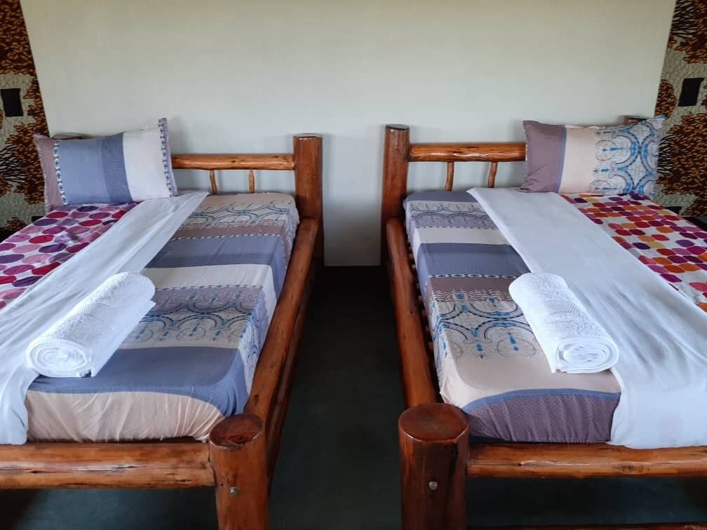 Two wooden beds with patterned bedding and rolled towels, separated by a wooden partition.