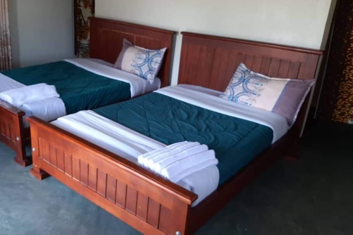 A room with two wooden beds, each with a green bedspread, white linens, and matching pillows.