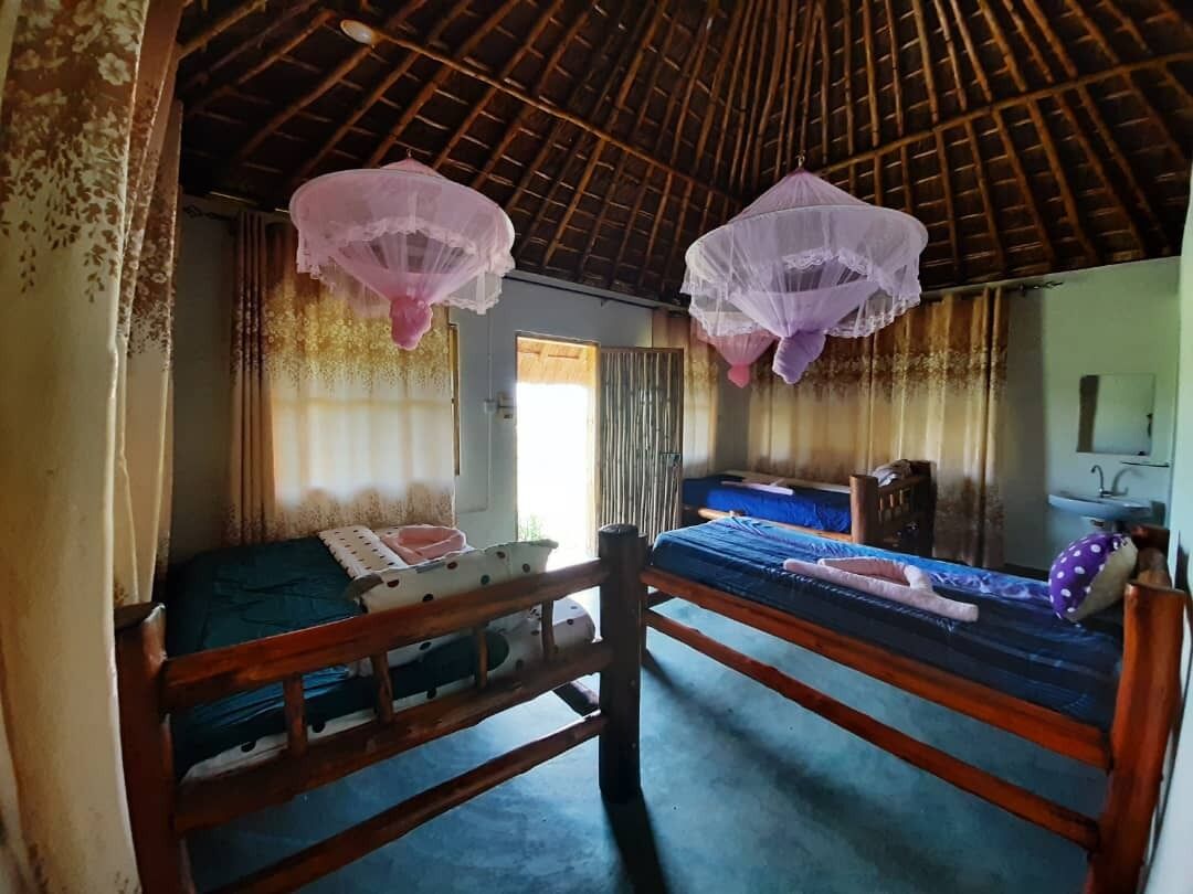 Una habitación con dos camas de madera, una ventana con cortinas, un espejo y un lavabo.