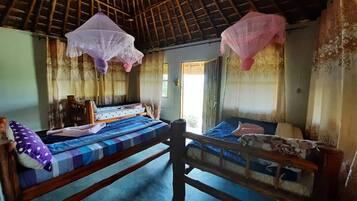 A rustic room with two wooden beds, a thatched roof, and mosquito nets hanging from the ceiling.