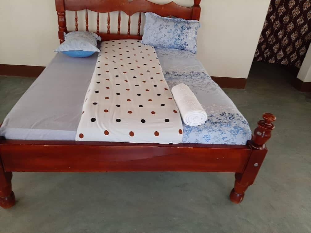 A wooden bed with a polka dot bedspread, a rolled-up blanket, and two pillows.