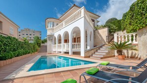 Una piscina con sillas de descanso y un edificio blanco con arcos.