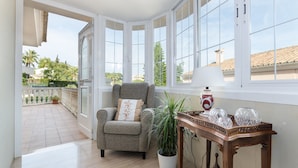 Una habitación con vistas a un patio con baldosas, un sillón gris con cojín, una planta en maceta y una mesa de madera con adornos.
