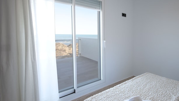 A room with a sliding glass door leading to a balcony with a view of the beach.
