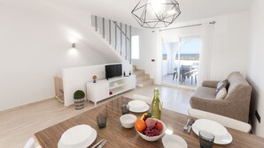 A modern living room with a staircase, a dining area with a wooden table, and a sofa.