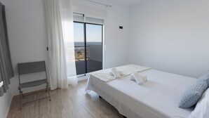 A bedroom with a bed, a chair, a balcony with a view, and a sliding door.