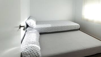 Una habitación pequeña con una cama individual, colcha blanca con estampado de estrellas y colchón blanco liso.