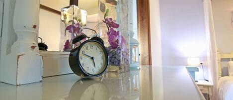 Un reloj sobre una mesa, con un jarrón de flores al fondo.
