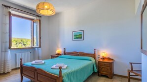 A bedroom with a wooden bed, two bedside lamps, a window with a view, and a framed picture on the wall. - Cosy apartment in villa for 5 people with WIFI, pool, TV, terrace, pets allowed and panoramic view (San Vivaldo)