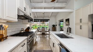 A modern kitchen with white cabinetry, a gas stove, and a large island with a sink. - LQ001 - 3 bedroom 3 bath with pool (La Quinta)